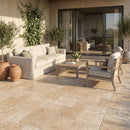 Outdoor patio with beige sofa, wooden coffee table, and chairs on a stone patio. Aspendos Tumbled Travertine Pavers