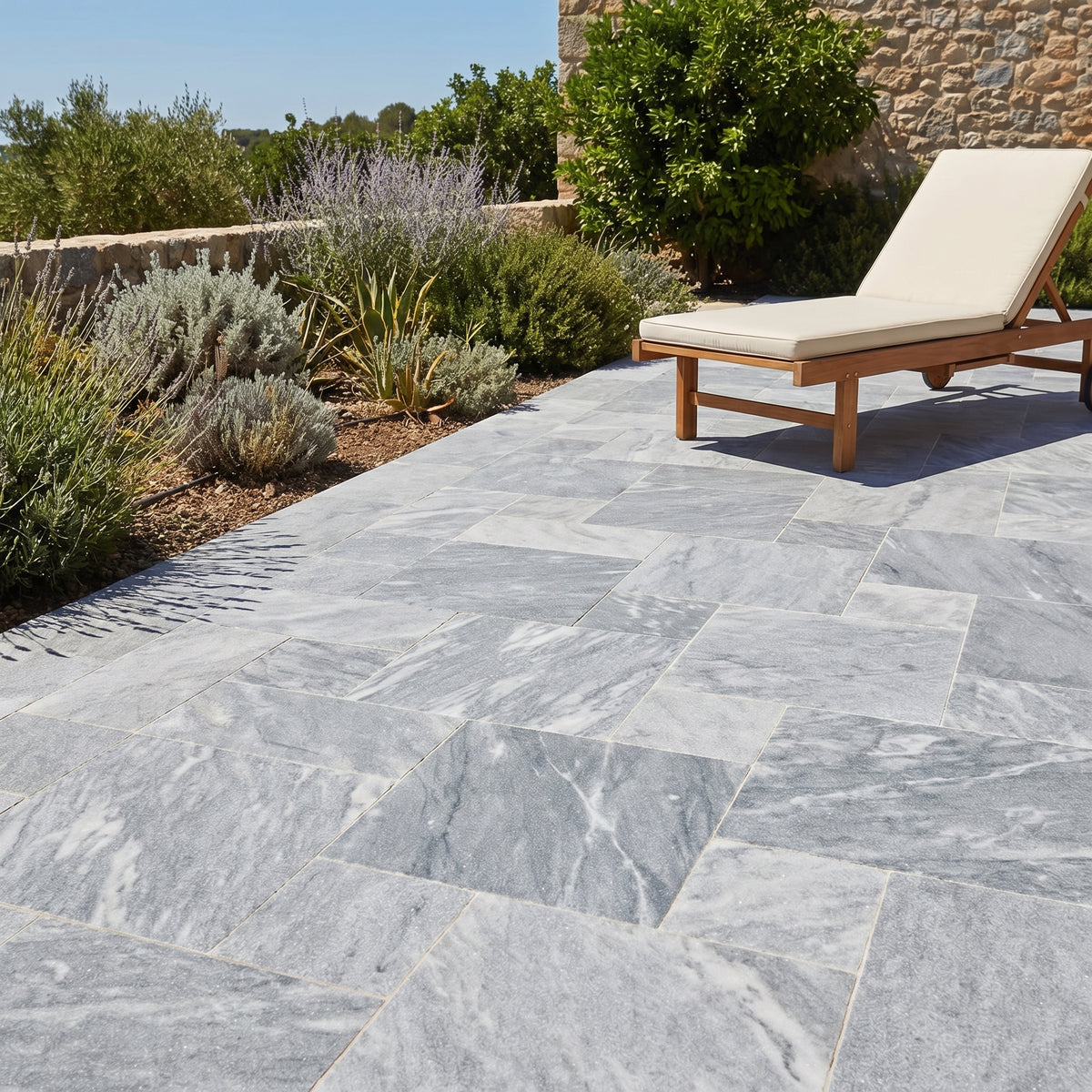 Outdoor patio with gray stone tiles, a wooden chair, and greenery. Bluestone tumbled pavers pattern