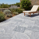 Outdoor patio with gray stone tiles, a wooden chair, and greenery. Bluestone tumbled pavers pattern