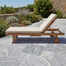 Wooden lounge chair with beige cushions on a stone patio with plants in the background. Bluestone tumbled pavers 