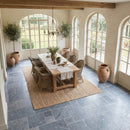 Dining room with wooden table and chairs, large windows, and decorative plants. Bluestone Sandblasted Brushed French Pattern Set Marble Tile