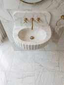 Marble sink with gold fixtures in a bathroom setting. Carrara White Marble Wall-mount Bathroom Sink Fluted Front (W)16" (L)24" (H)6"