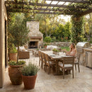 Outdoor patio with dining table, chairs, and a fireplace under a pergola. Country Classic Travertine Tumbled Pavers