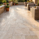 Outdoor patio with stone tiles, wicker furniture, and potted plants. Travertine Miletos Ivory Tumbled Pavers