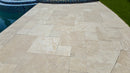 Beige stone tiles on a patio next to a pool. Ivory Moderno Travertine Filled and Tumbled Pavers