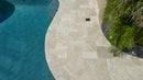 Beige stone pathway leading to a pool with greenery on the side. Ivory Moderno Travertine Filled and Tumbled Pavers