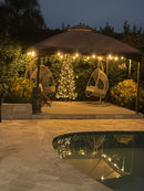 Gazebo with string lights, wicker chairs, and a Christmas tree by a pool at night. Aspendos Tumbled Travertine Pavers