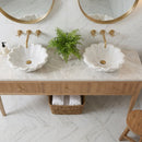 Bathroom vanity with two white sinks, gold fixtures, and a plant on a marble floor.