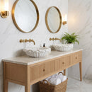Bathroom vanity with marble countertop, gold fixtures, and round mirrors on a marble wall.