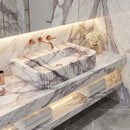 Marble bathroom vanity with sink and decorative items against a marble wall.