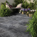 Outdoor patio with gray tiles, green plants, and a bench. Silver Shadow Marble Tumbled Pavers (3cm Thickness)