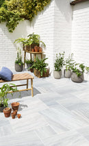 Outdoor patio with potted plants and a wooden bench against a white brick  Solto White Marble Leathered Paverswall.